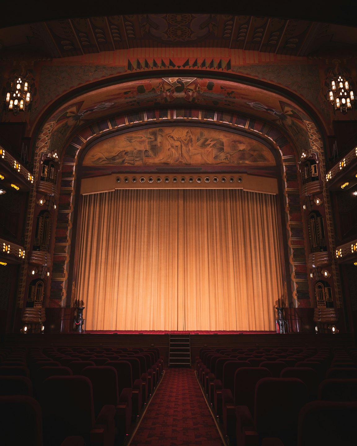 Tenda dorata chiusa davanti a poltrone vuote di velluto rosso in un teatro d'epoca.